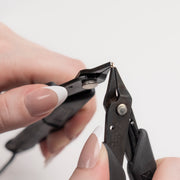 Close-up of hands using a pair of black pliers on a white background