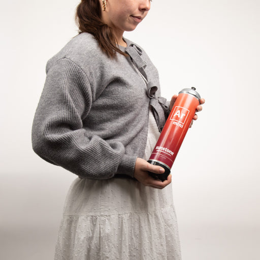 Person holding a portable red and black argon gas canister with a logo on a plain background