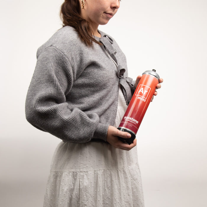 Person holding a portable red and black argon gas canister with a logo on a plain background