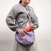 Person wearing a gray sweater and holding a purple bag with a red argon mini tank in it.